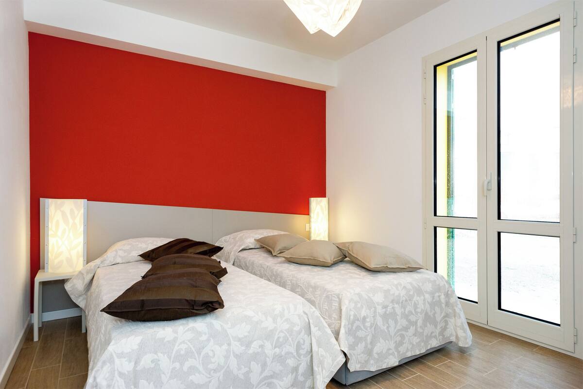A hotel room with two beds, a red accent wall, and a large window.