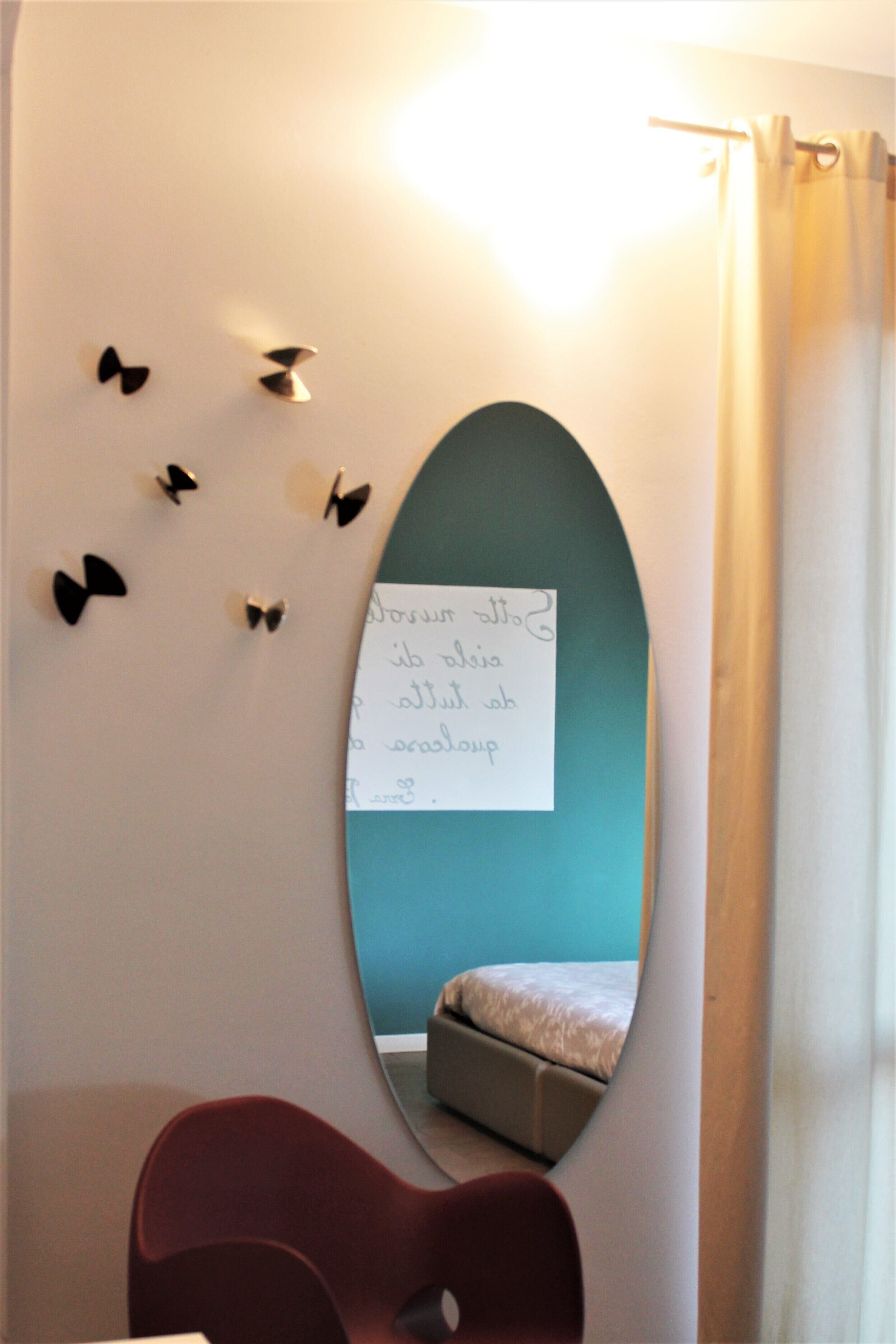 A room with a teal accent wall, a mirror reflecting a bed, and a note on the wall.