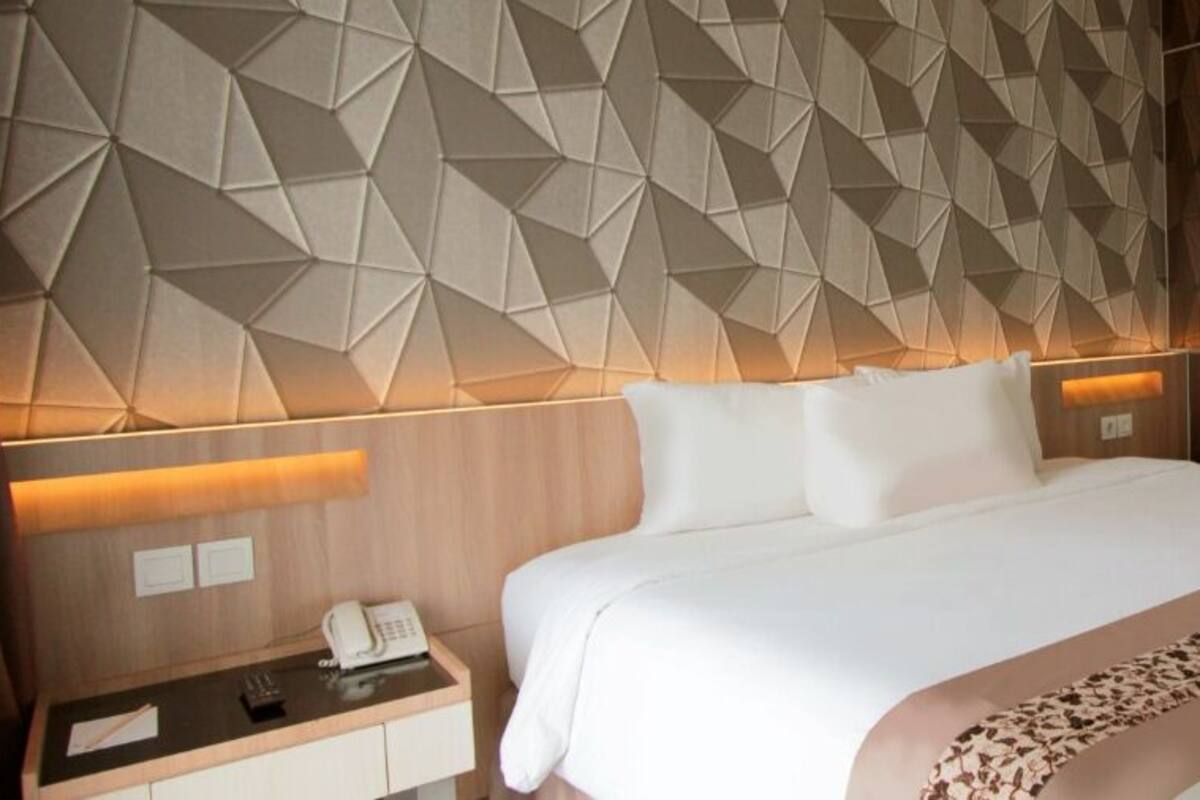 Moderni hotellihuone, jossa on geometrisesti kuvioitu sängynpääty, siististi pedattu sänky koristeellisella päiväpeitteellä sekä yöpöytä, jossa on puhelin ja lamppu.
