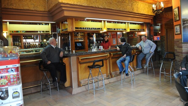 A bar area with stools, a counter, and a person standing behind the bar. - Hostal Venecia (Azagra)
