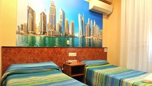 A hotel room with two beds, a cityscape mural on the wall, an air conditioning unit, and a nightstand with a phone. - Hostal Venecia (Azagra)