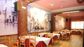 A restaurant with multiple tables and chairs, a large mural on the wall, and a tiled floor. - Hostal Venecia (Azagra)