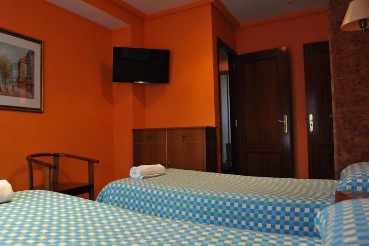 A hotel room with two beds, a television, a painting, and a wooden wardrobe.