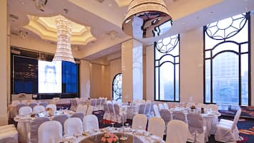 A banquet hall with round tables, white chairs, and a large chandelier.