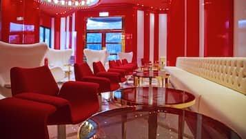 A modern hotel lobby with red and white furnishings, a central round table, and a large chandelier.