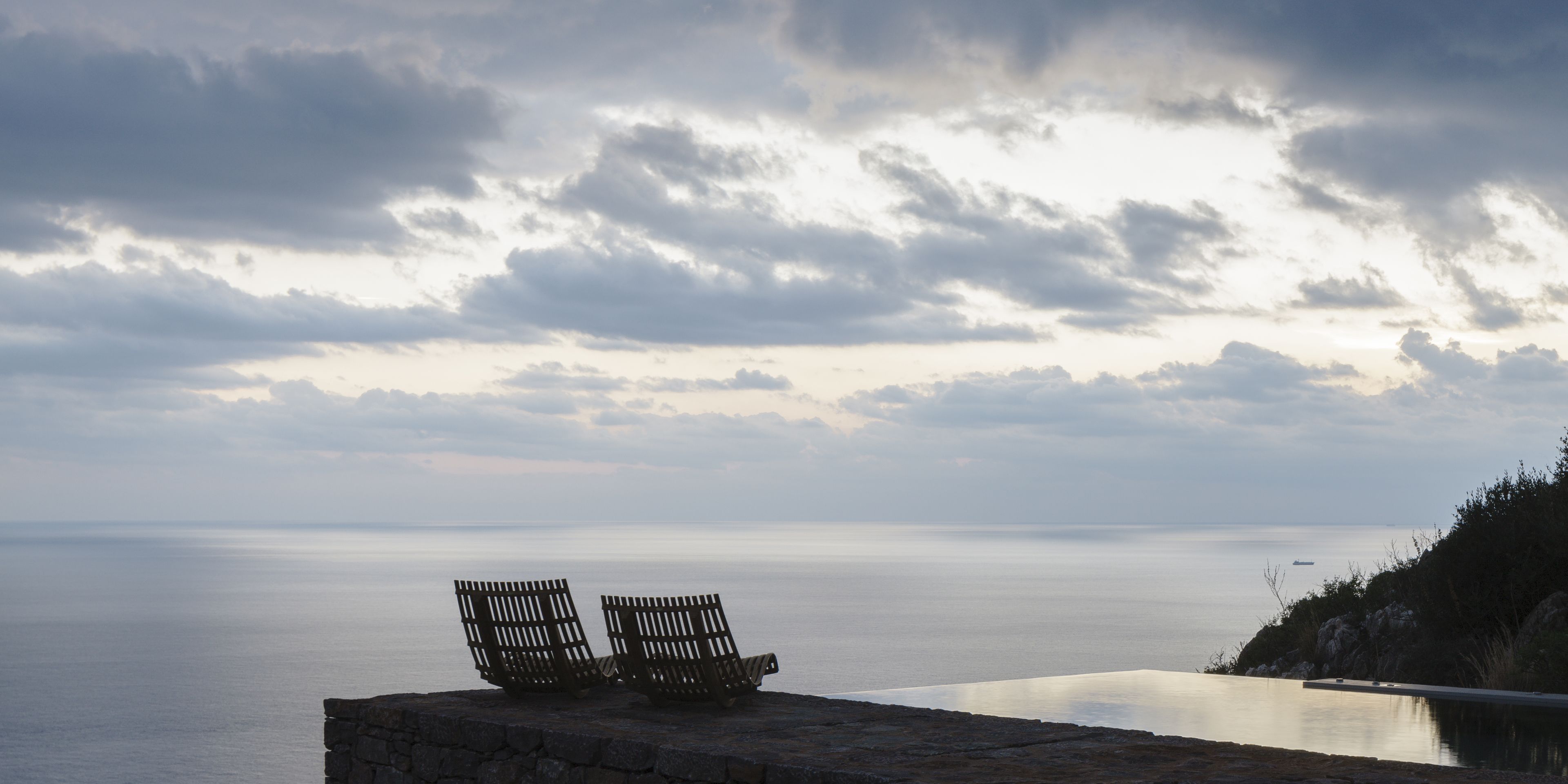 A stone bench overlooking a calm sea with a cloudy sky.