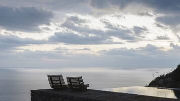 A stone bench overlooking a calm sea with a cloudy sky.