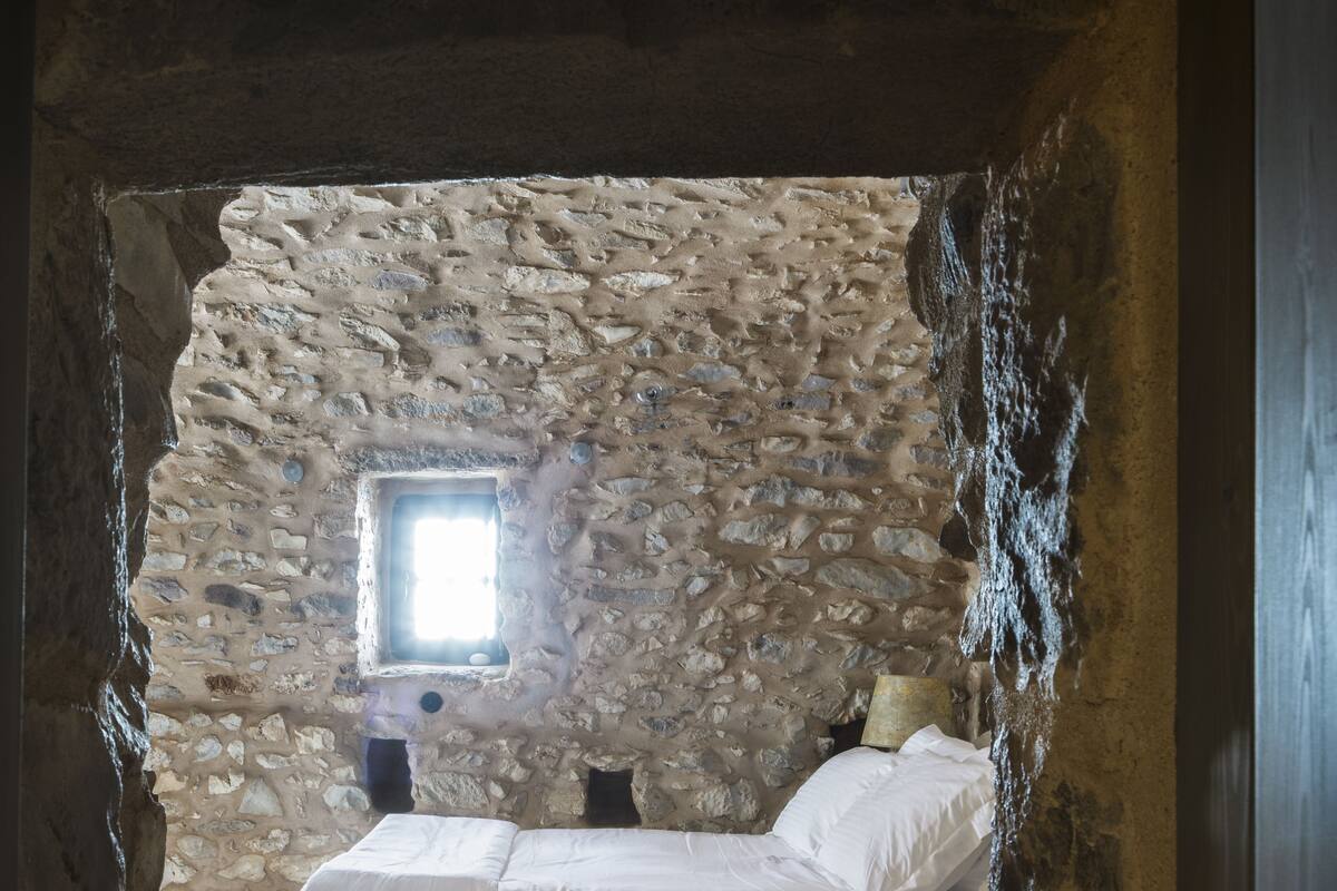 Ein Schlafzimmer mit Steinwand, kleinem Fenster, Bett und Nachttisch.