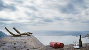 Un saliente de piedra con una botella de vino, copas y una toalla enrollada, con vistas a una masa de agua tranquila y montañas lejanas.