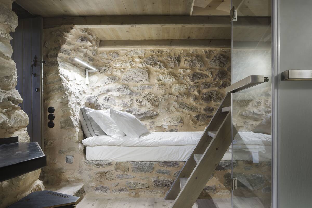 Ein Schlafzimmer mit Steinsturz, einem Bett mit weißer Bettwäsche, einer Holzleiter und einem kleinen Tisch.