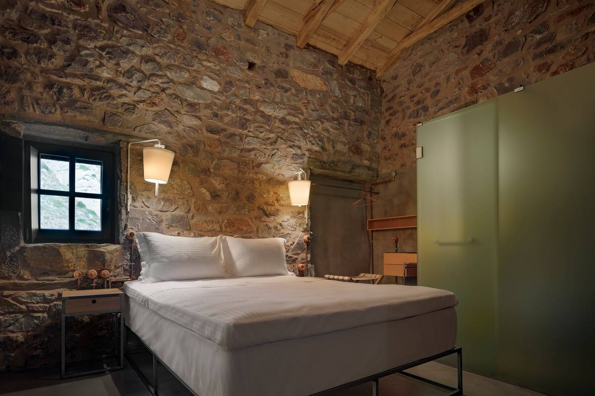 Ein Schlafzimmer mit Steinwand, einem Bett, Nachttischen und einem Kleiderschrank.