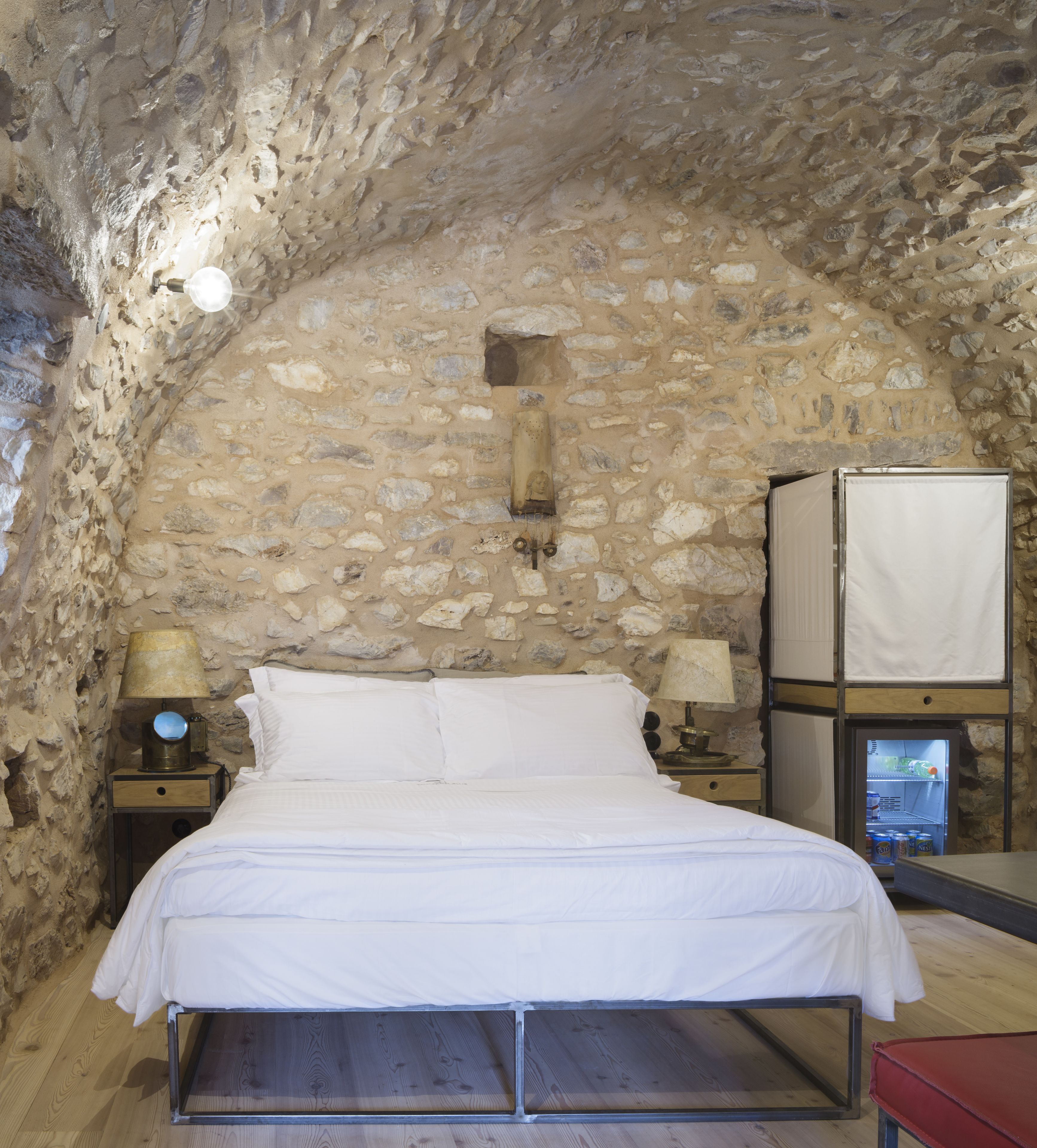 A stone-walled bedroom with a bed, two bedside tables with lamps, and a television.