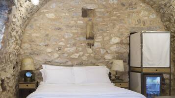 A stone-walled bedroom with a bed, two bedside tables with lamps, and a television.