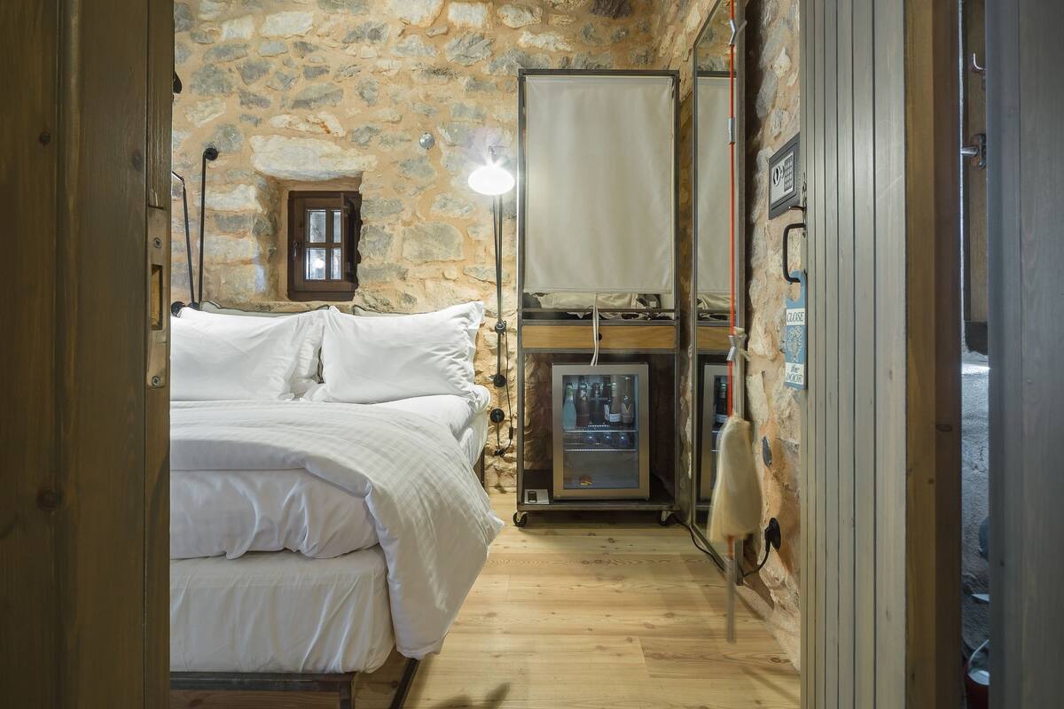 Ein Schlafzimmer mit Steinwand, Holzboden, einem Bett, einem Nachttisch, einer Lampe und einem Kamin.