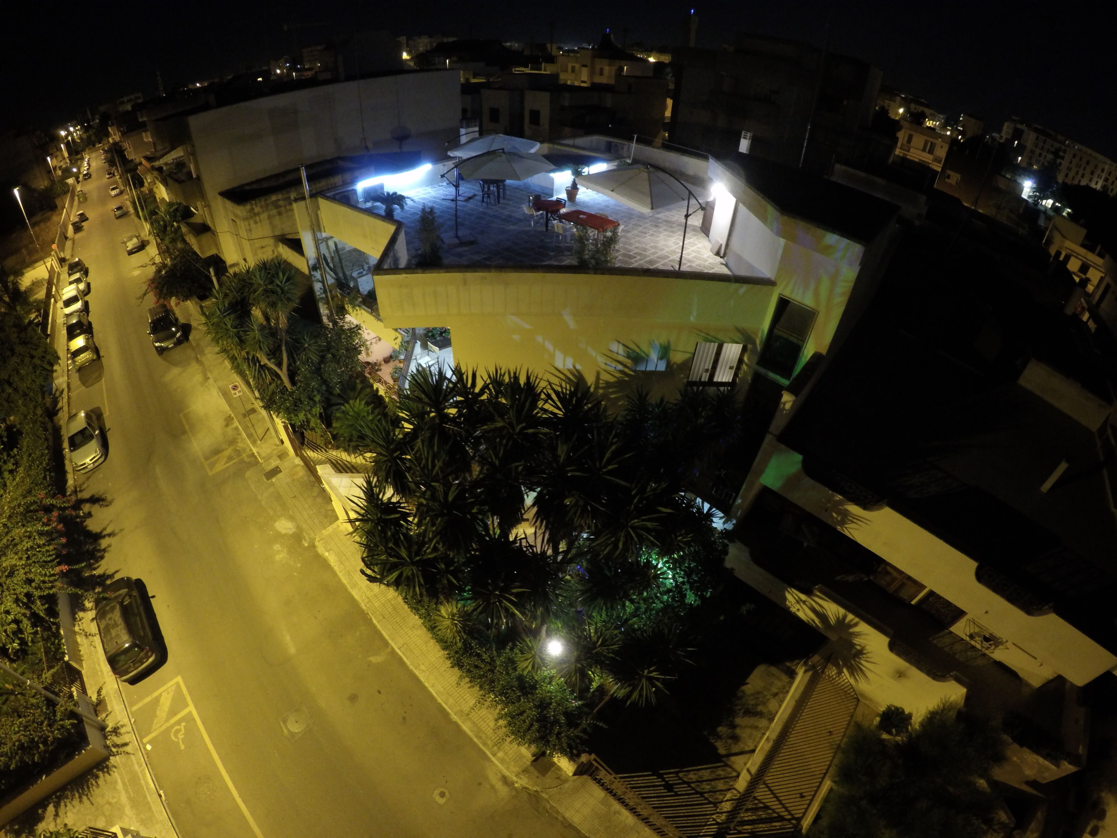 An aerial view of a building with a rooftop terrace, parking area, and surrounding vegetation.