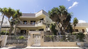 Un edificio residencial de varios pisos con balcones, una entrada porticada y palmeras.
