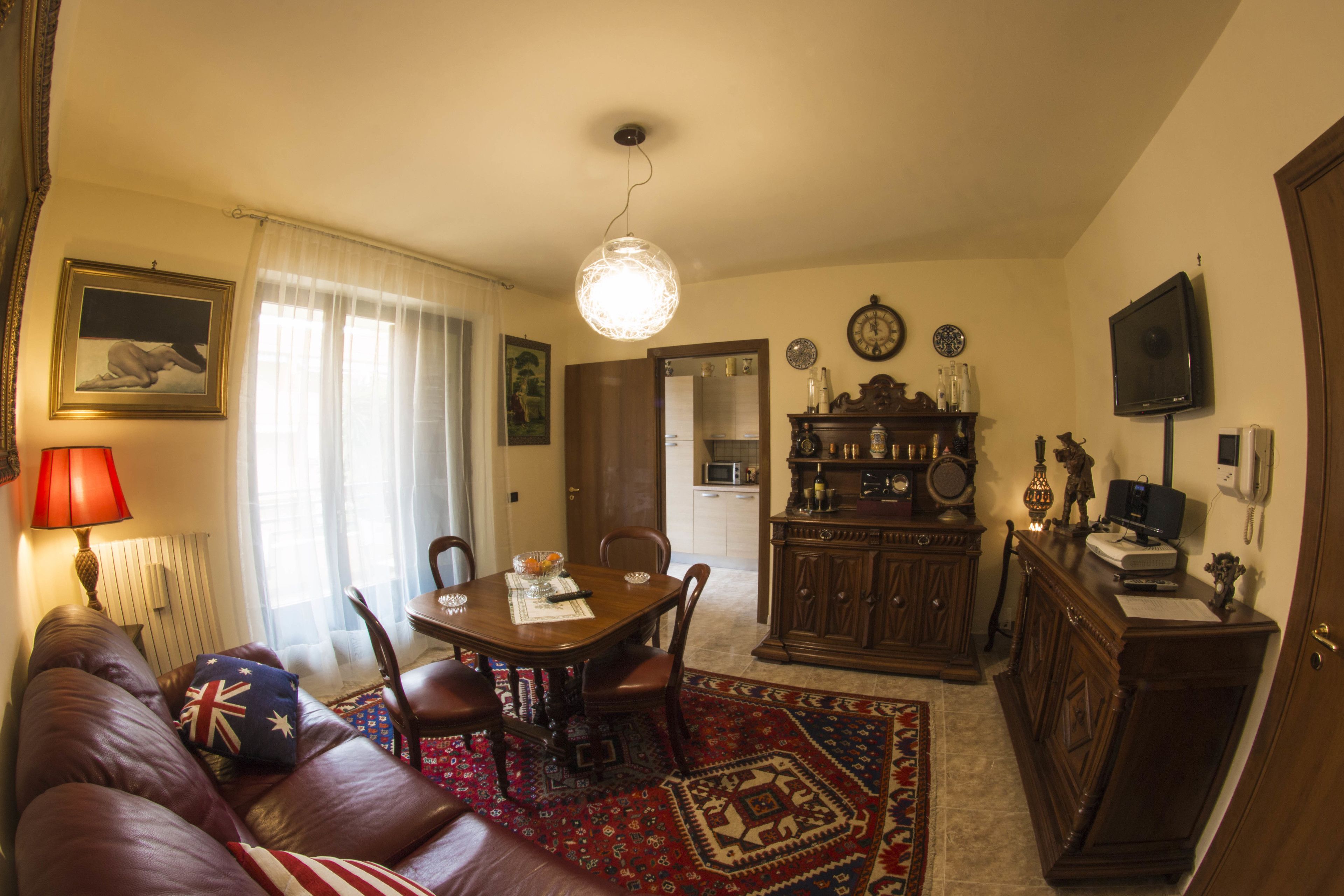 A living room with a brown leather sofa, a wooden dining table, and a kitchen area in the background.
