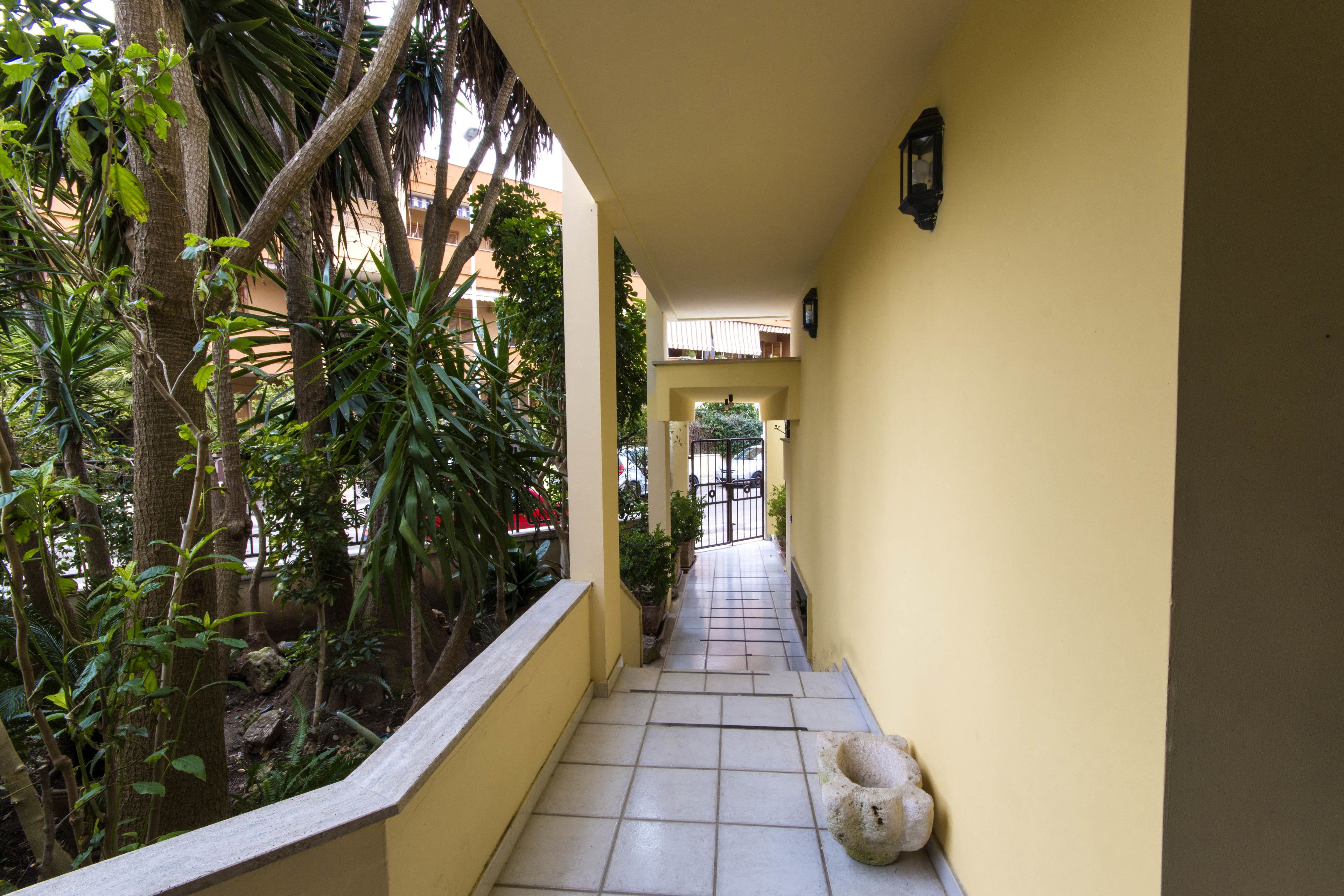 A narrow corridor with yellow walls, tiled flooring, and potted plants.