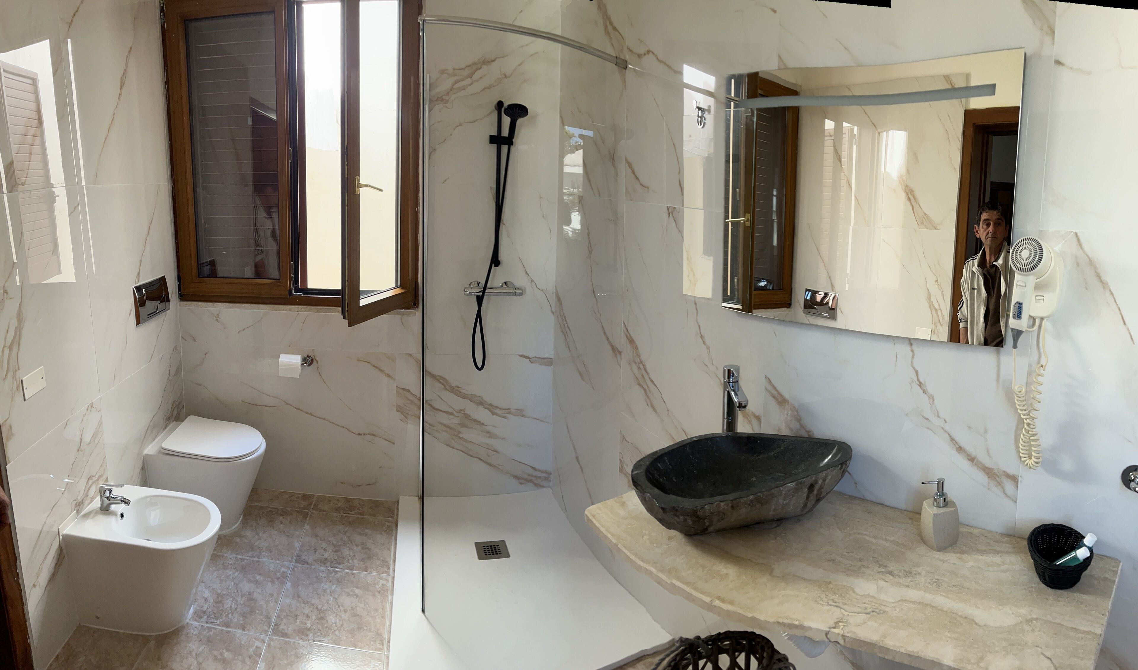 A modern bathroom with a glass-enclosed shower, a white toilet, a bidet, and a black sink.