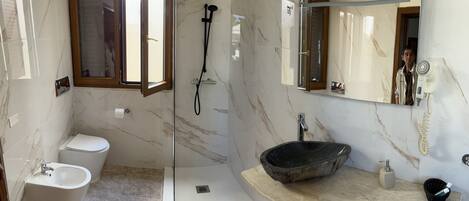 A modern bathroom with a glass-enclosed shower, a white toilet, a bidet, and a black sink.