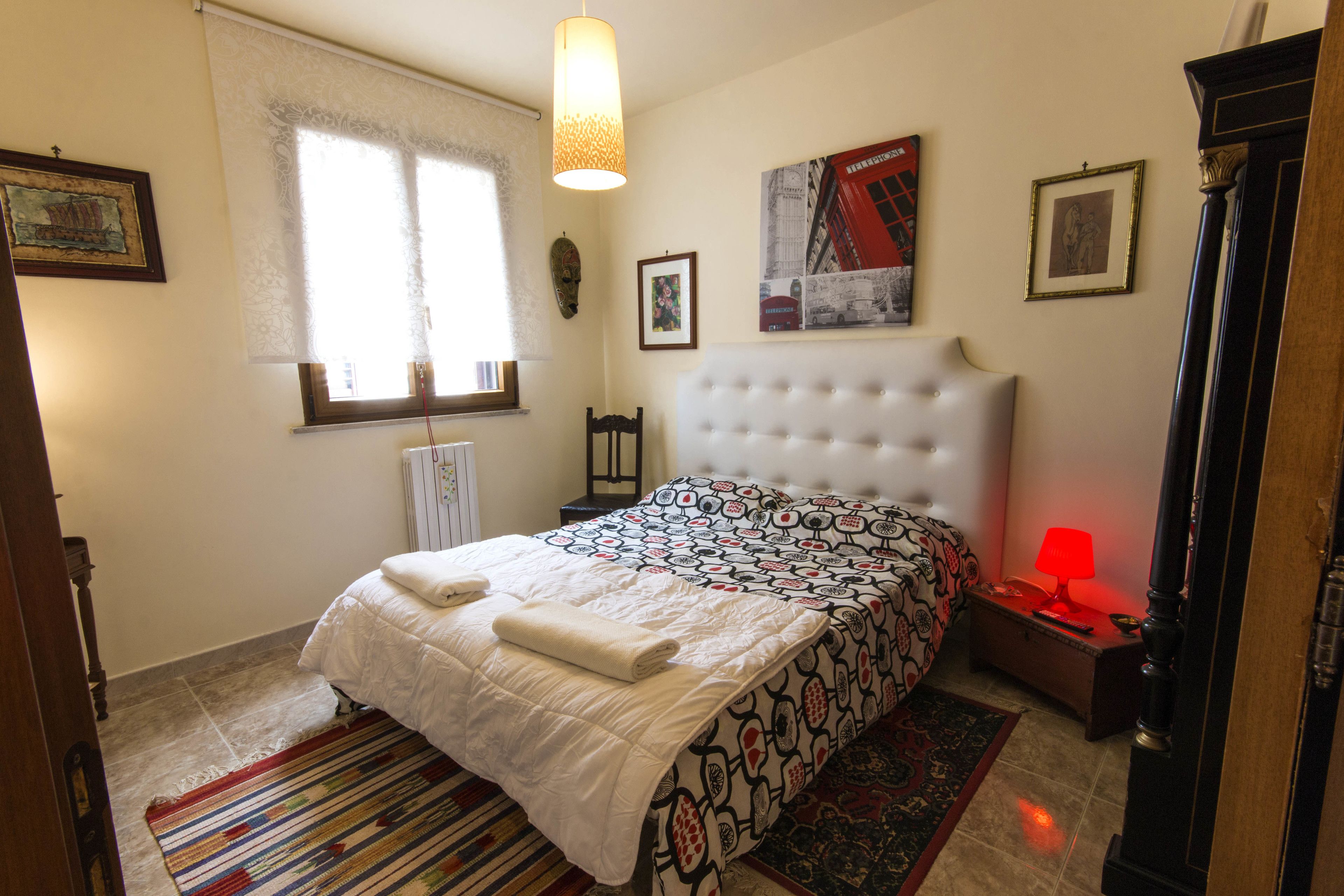 Un dormitorio con cama, mesita de noche, lámpara y ventana con cortinas.