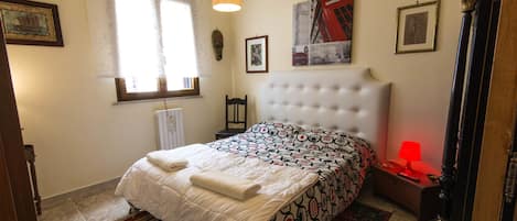 Un dormitorio con cama, mesita de noche, lámpara y ventana con cortinas.