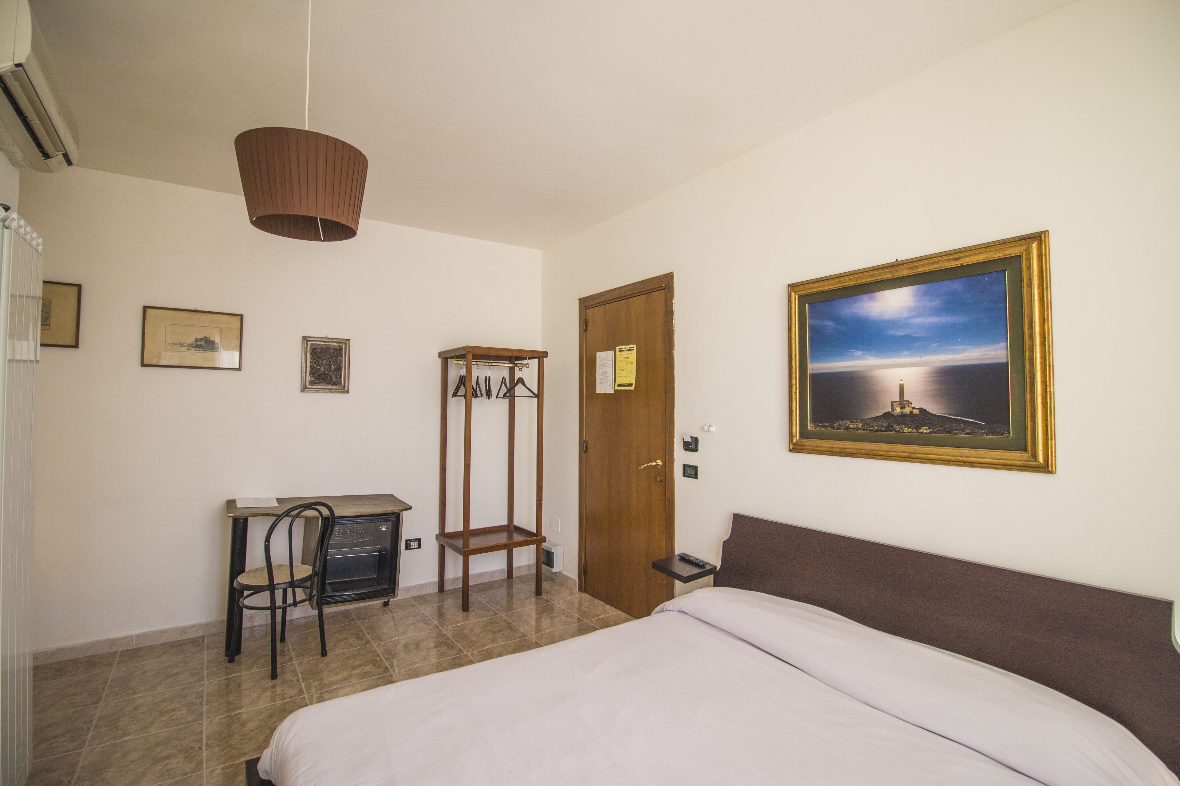 A bedroom with a bed, a desk with a chair, a wardrobe, and a painting on the wall.