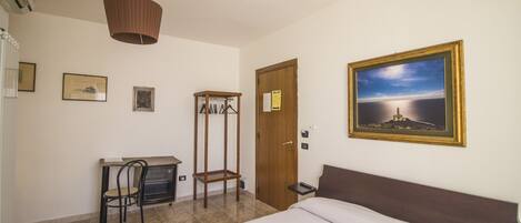 A bedroom with a bed, a desk with a chair, a wardrobe, and a painting on the wall.