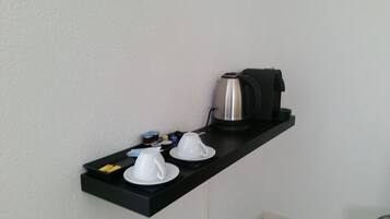 A black shelf with a coffee maker, two white cups, and a small tray with condiments.