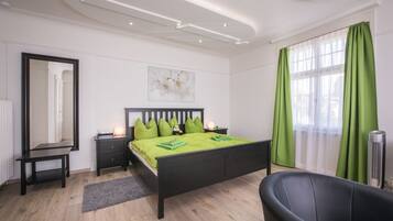A modern bedroom with a black bed, green bedding, a bedside table, a mirror, a nightstand, a lamp, a chair, and a window with green curtains.