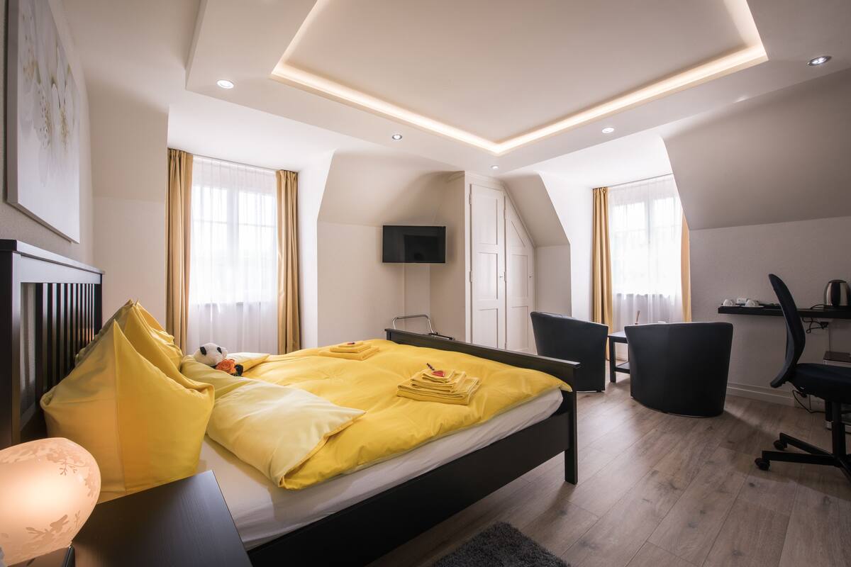 A modern hotel room with a large bed, a desk, a chair, and a TV.