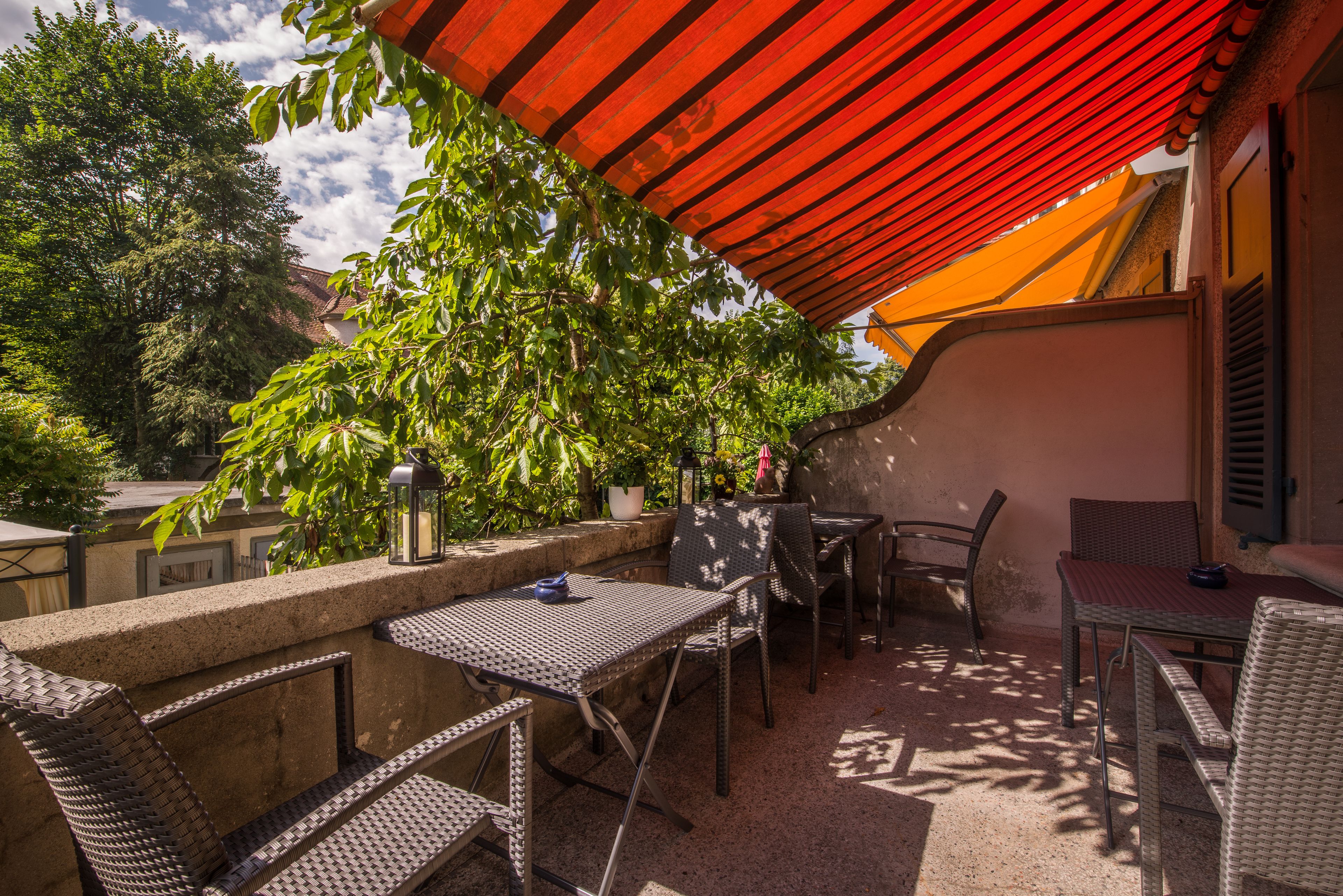 Une terrasse extérieure avec des meubles en osier, un auvent rouge et des plantes en pot.