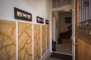 Un pasillo con pared texturizada, una puerta de madera y una escalera al fondo.