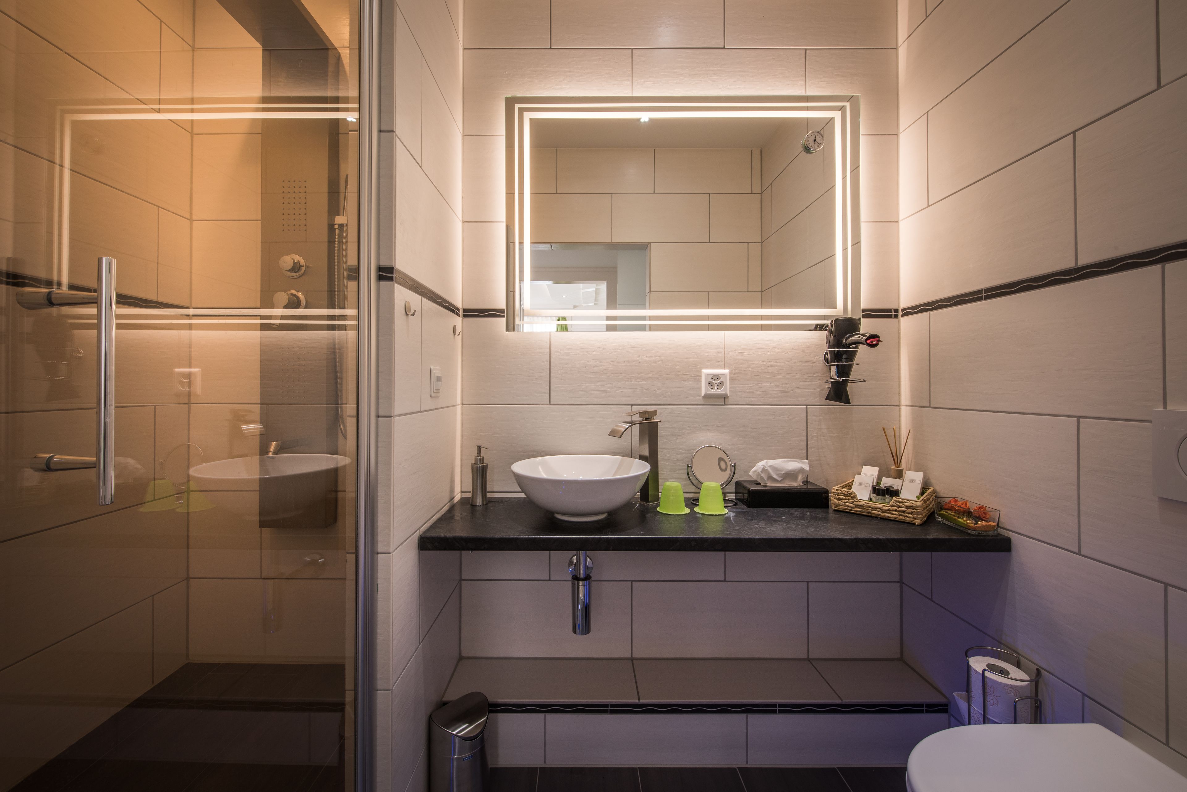A modern bathroom with a glass-enclosed shower, a white sink, and a mirror with integrated lighting.