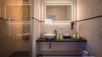 A modern bathroom with a glass-enclosed shower, a white sink, and a mirror with integrated lighting.