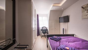 A bedroom with a bed, a desk, a chair, a TV, and a mirror.