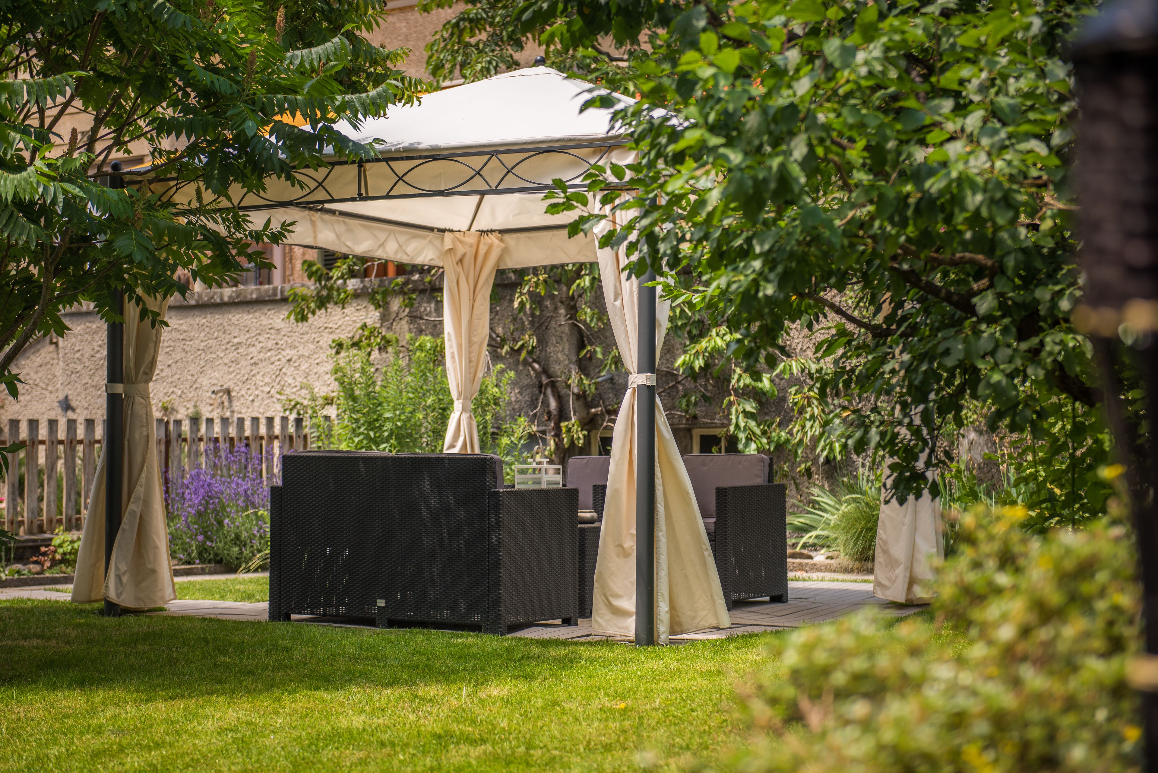 An outdoor patio area with a covered seating arrangement and a stone wall in the background.