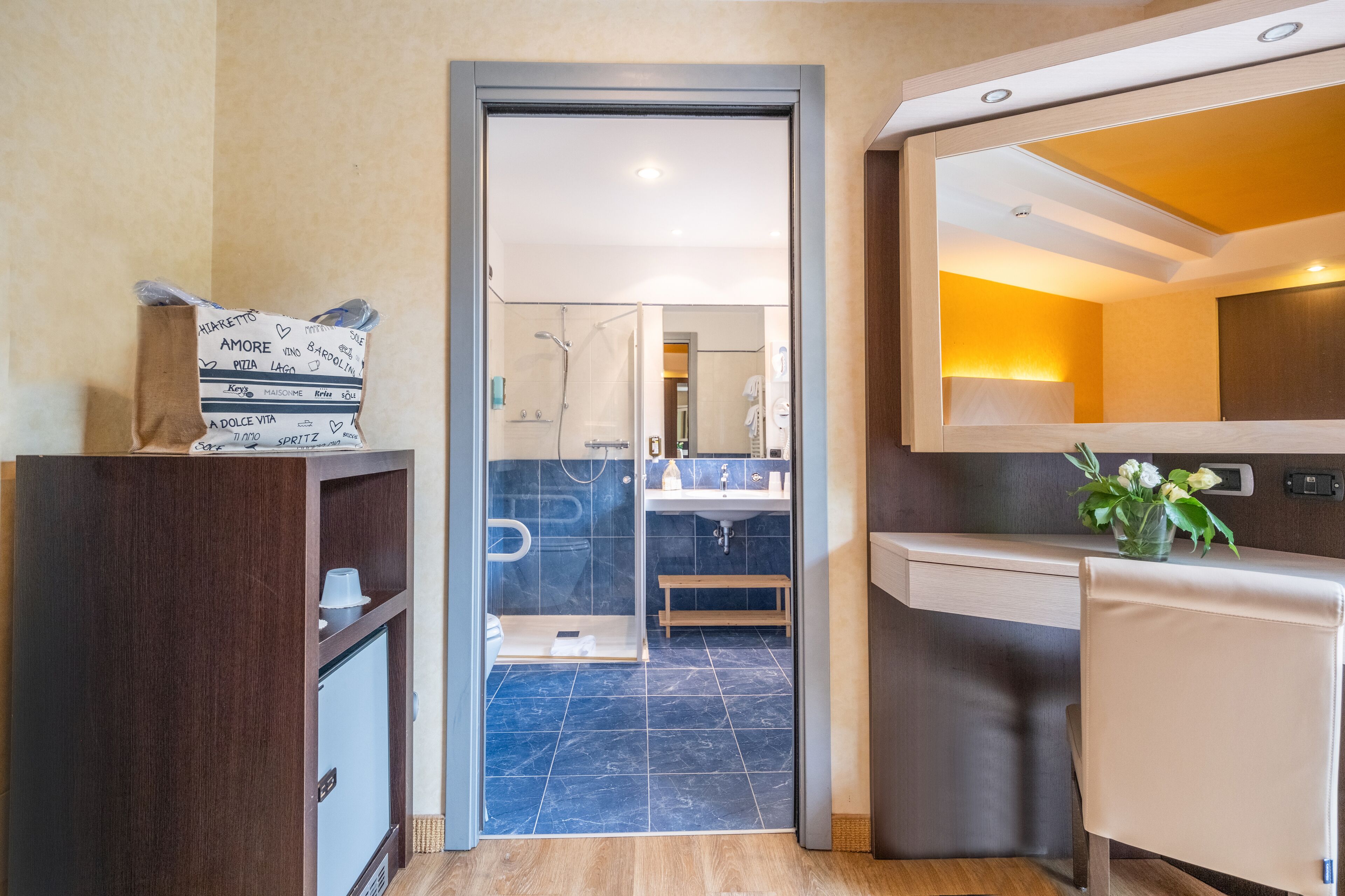 A modern bathroom with a shower, sink, and mirror. There is a wooden cabinet with a towel and a small plant on the counter.