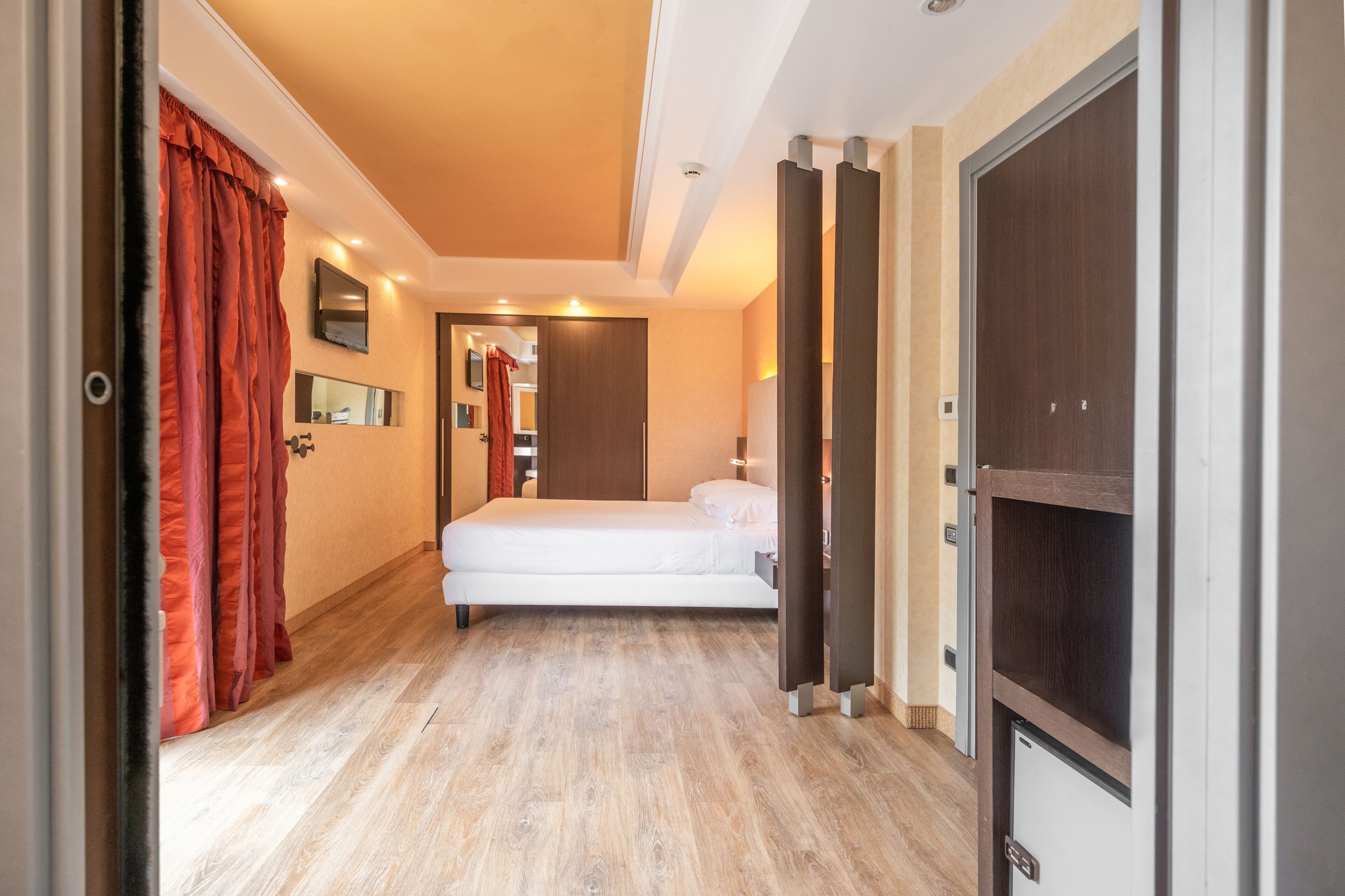 A modern hotel room with a wooden floor, a bed, a wardrobe, and a mirror.