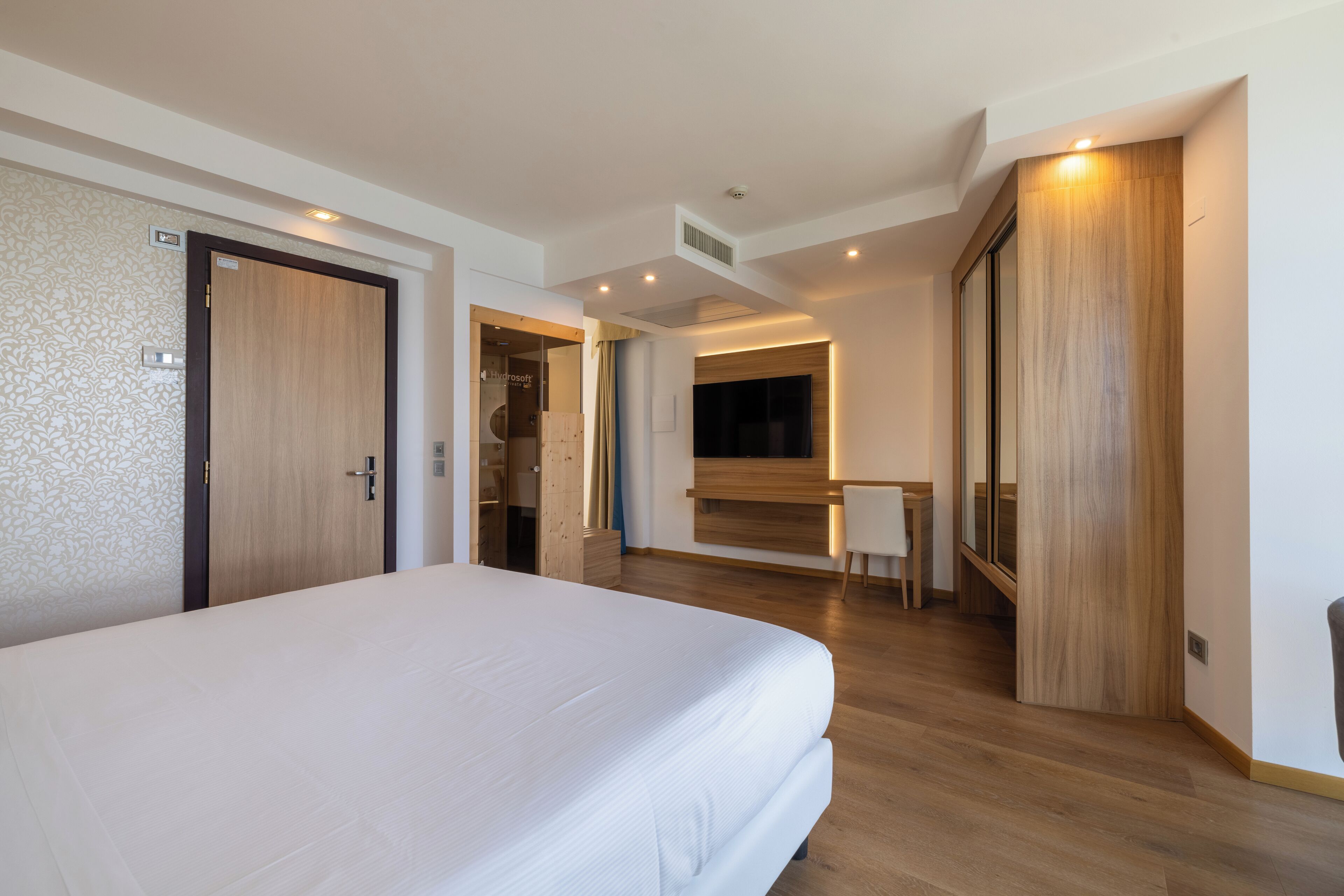 Una habitación de hotel moderna con una cama grande, suelo de madera, un escritorio y un armario.