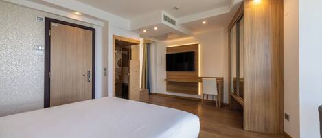 Una habitación de hotel moderna con una cama grande, suelo de madera, un escritorio y un armario.