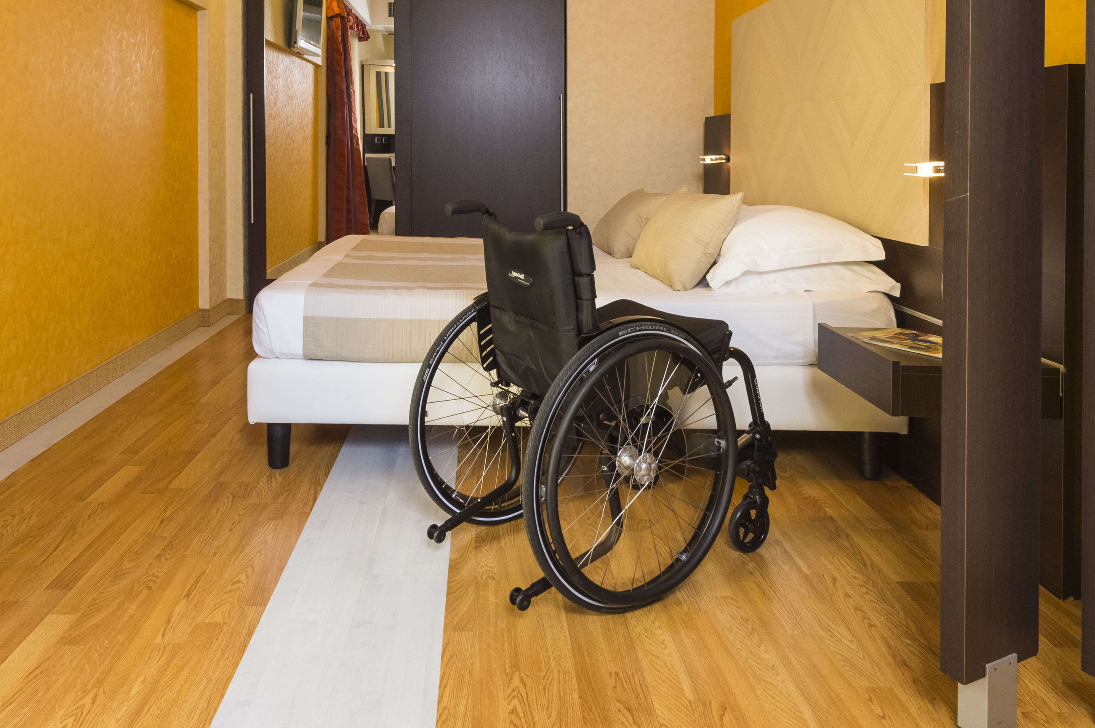 Habitación de hotel con silla de ruedas, cama y mesita de noche.