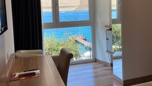 Une chambre d’hôtel avec un bureau en bois, une chaise, un lit, une télévision et une grande fenêtre donnant sur la mer et un quai.