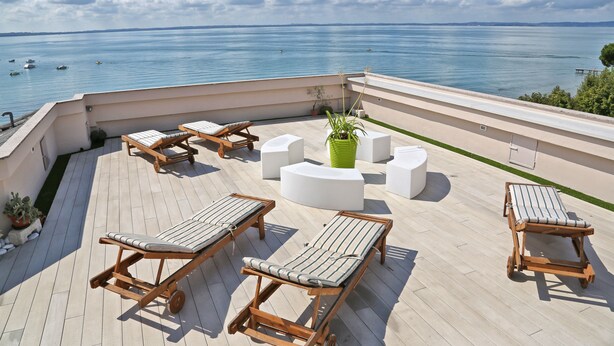 Une terrasse sur le toit, dotée de chaises longues en bois, d’un espace salon central et offrant une vue sur la mer.