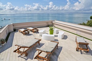 Eine Dachterrasse mit Holzliegen, einer zentralen Sitzecke und Blick aufs Meer.