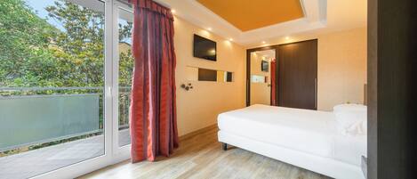 A modern bedroom with a large sliding glass door to a balcony, a white bed, and a flat-screen TV mounted on the wall.