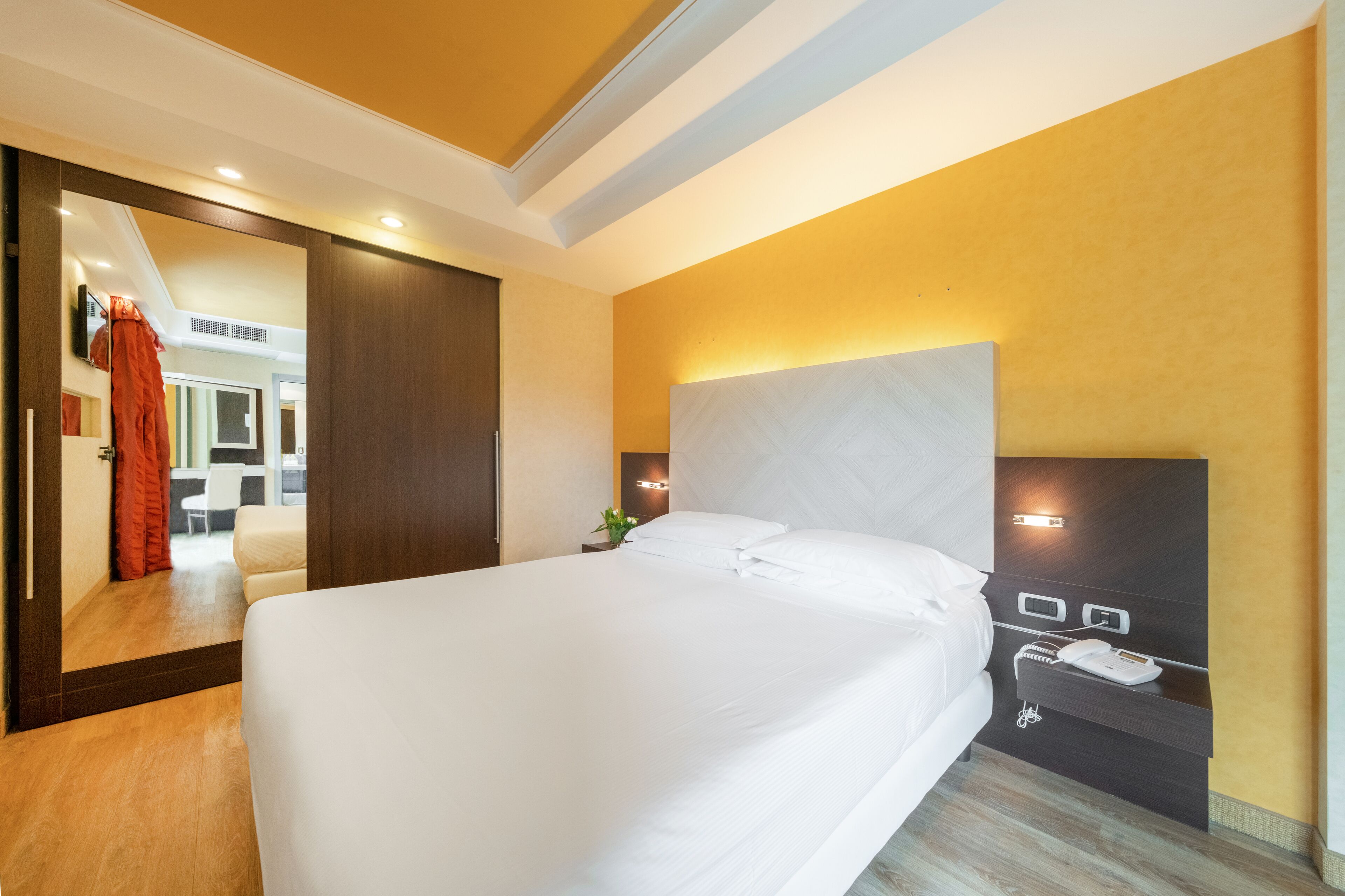 Une chambre d’hôtel avec un grand lit, une table de chevet avec un téléphone et une lampe, et un miroir au mur.
