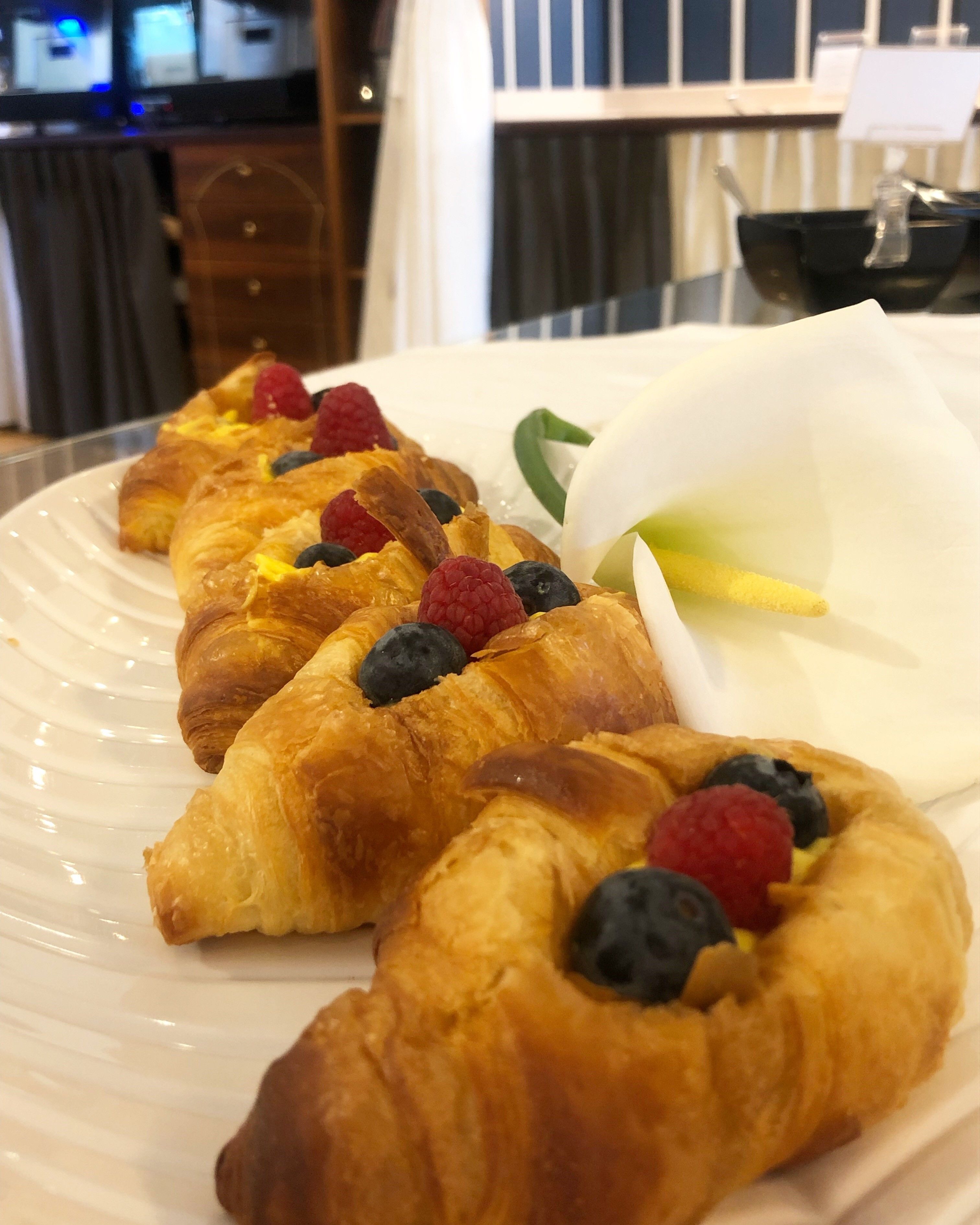 Une assiette de croissants, garnis de fruits rouges et surmontée d’une fleur blanche.