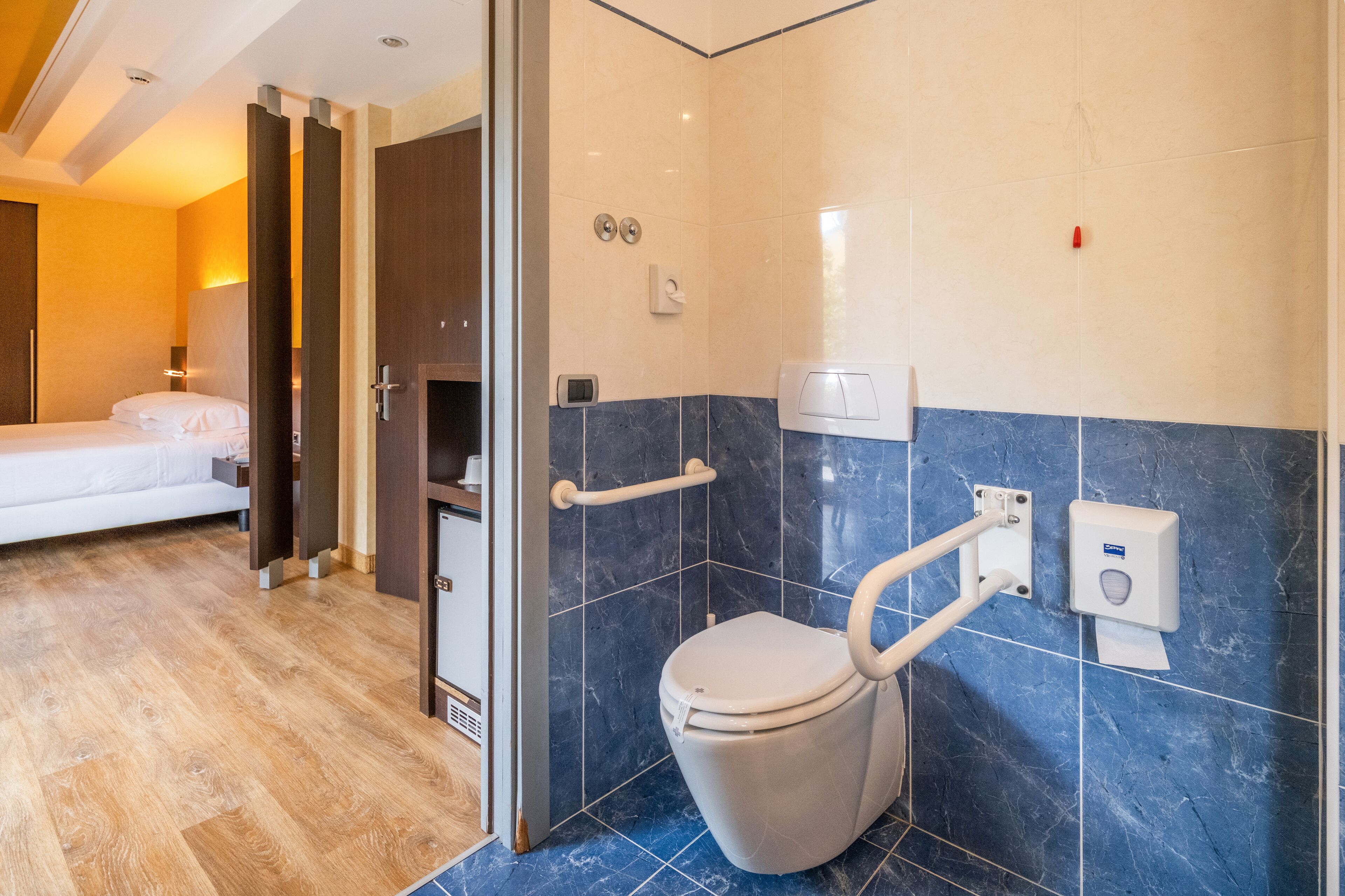 Un baño moderno con inodoro, barras de apoyo y dispensador de gel antibacterial.