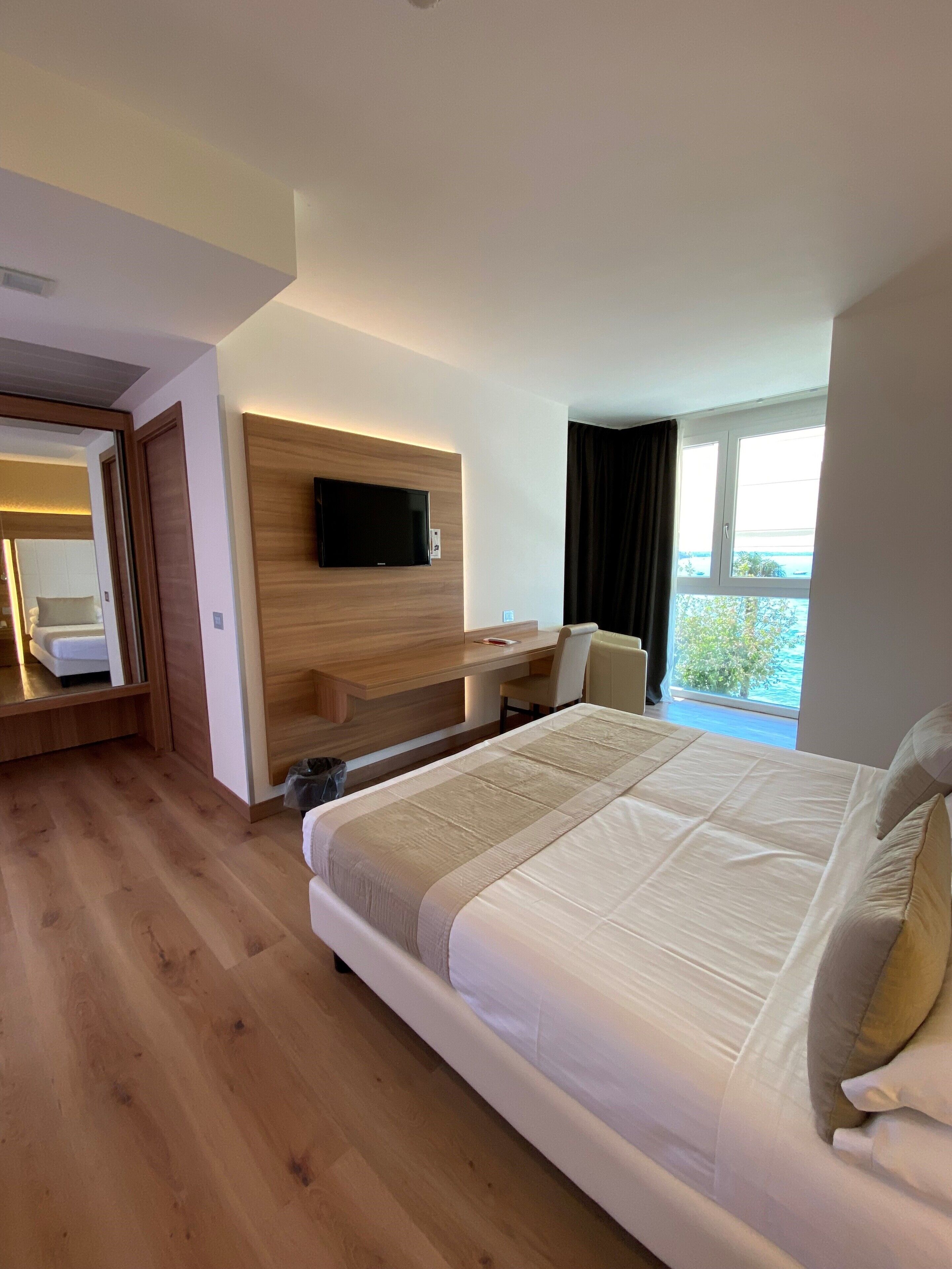 A modern hotel room with a large bed, a desk with a flat-screen TV, and a balcony with a view.